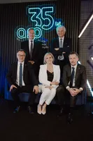 Portret pięciu osób w strojach biznesowych na tle neonu „35 lat arp”. Trzy osoby siedzą na kanapie, a dwaj mężczyźni stoją za nimi w tle.