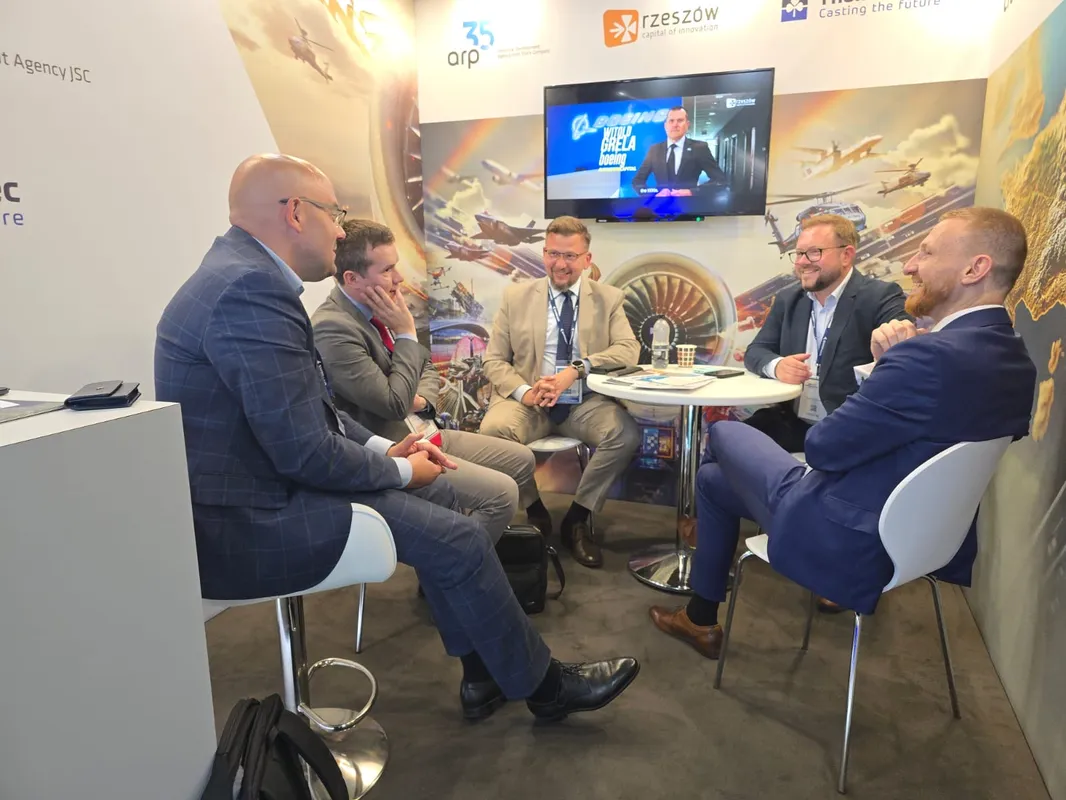 Kilka osób prowadzi spotkanie przy stoliku na stoisku wystawowym podczas Farnborough International Airshow 2026.