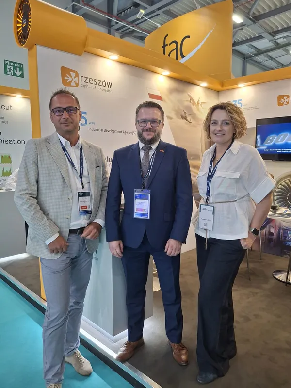 Trzy osoby stoją przy stoisku promującym Rzeszów i Podkarpacie podczas Farnborough International Airshow 2026, na tle materiałów dotyczących przemysłu lotniczego i inwestycji.