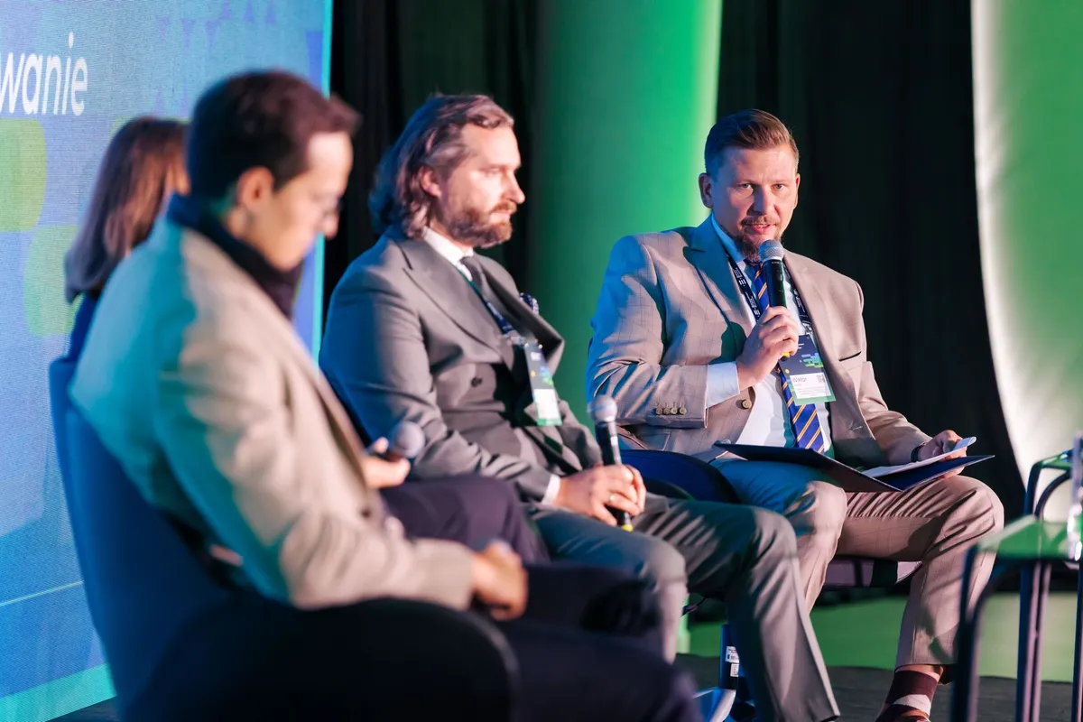 Mężczyzna z mikrofonem zabiera głos podczas panelu „Dual-use: jak sfinansować skalowanie polskich technologii?” na Carpathian Drone Summit 2026, obok pozostałych uczestników dyskusji.