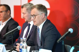 Łukasz Kotapski, Wiceprezes ARP S.A., przemawia do mikrofonu podczas panelu dyskusyjnego na tle czerwonej ścianki reklamowej.
