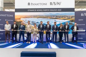 Przedstawiciele BSH, Panattoni i partnerów stoją w jednym rzędzie na scenie, trzymając wstęgę podczas ceremonii otwarcia nowej fabryki małego AGD w Rudnej Wielkiej, na tle wizualizacji zakładu