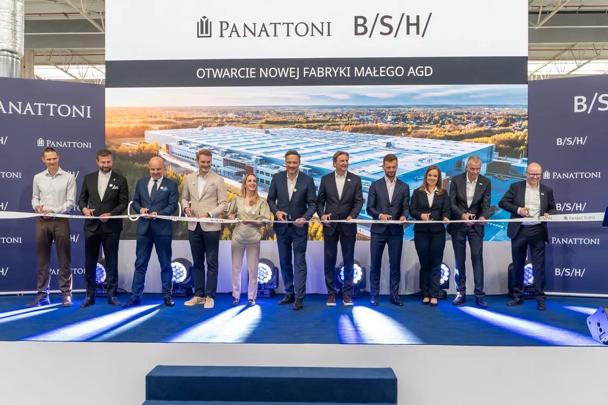 Przedstawiciele BSH, Panattoni i partnerów stoją w jednym rzędzie na scenie, trzymając wstęgę podczas ceremonii otwarcia nowej fabryki małego AGD w Rudnej Wielkiej, na tle wizualizacji zakładu