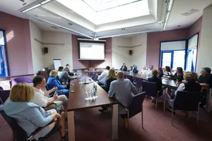 Uczestnicy spotkania w szerokim ujęciu sali konferencyjnej, z widocznym ekranem projekcyjnym z przodu.