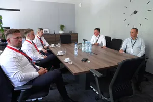 Spotkanie robocze pięciu mężczyzn w garniturach i koszulach wokół drewnianego stołu konferencyjnego.
