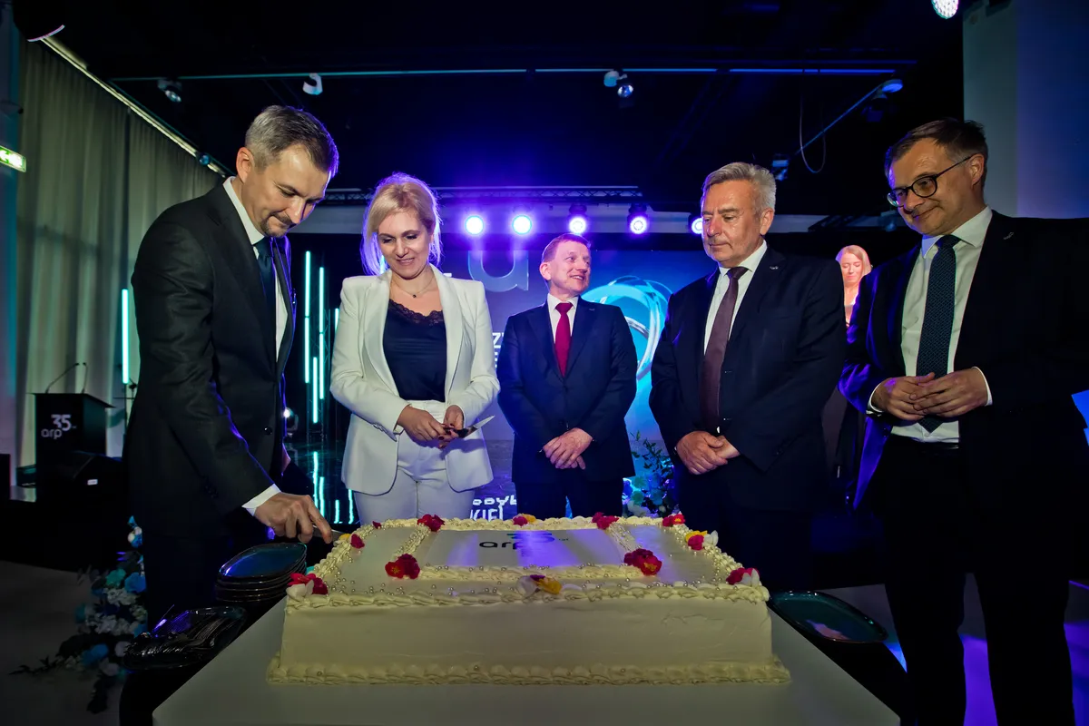 Pięć osób w strojach biznesowych kroi duży jubileuszowy tort z logo ARP na scenie. W tle widoczne jest nowoczesne, niebieskie oświetlenie eventowe oraz fragmenty dekoracji.