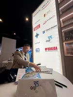 Dyrektor SSE EURO-PARK MIELEC, sięga po materiały informacyjne na stoisku Aviation Valley podczas Aerospace & Defense Meetings Sevilla 2026, obok podświetlanej ścianki z logotypami firm branży lotniczej.