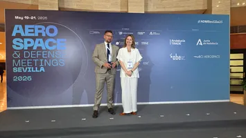 Mężczyzna i kobieta stoją na scenie przed ścianką z logotypami organizatorów i hasłem Aerospace & Defense Meetings Sevilla 2026.